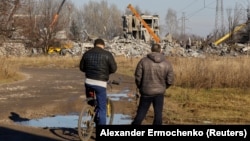 Two men watch workers removing the debris of the building in Makiyivka where the Russian soldiers were housed when the strike hit on New Year's Eve.