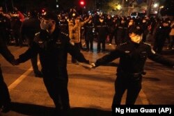 Polițiști chinezi formează o linie pentru a opri protestatarii care mărșăluiesc în Beijing, duminică, 27 noiembrie 2022.