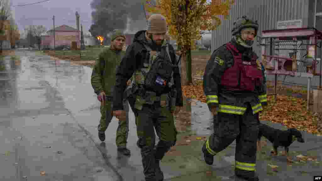 Az ukrán mentőszolgálat egyik tagja és egy katona ellenőrzi a területet, miközben fekete füst száll fel egy olajtároló elleni támadás után Herszonban.&nbsp;