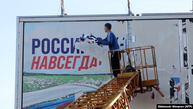 Рабочий срывает рекламный щит с надписью "Россия здесь навсегда" в освобожденном ВСУ Херсоне, 14 ноября