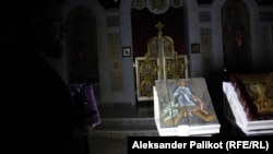 Sveštenik Andrij Dudčenko pokušava da osvijetli ikone koje su na kutijama za municiju naslikali ukrajinski umjetnici Oleksandr Klimenko i Sofia Atlantova.