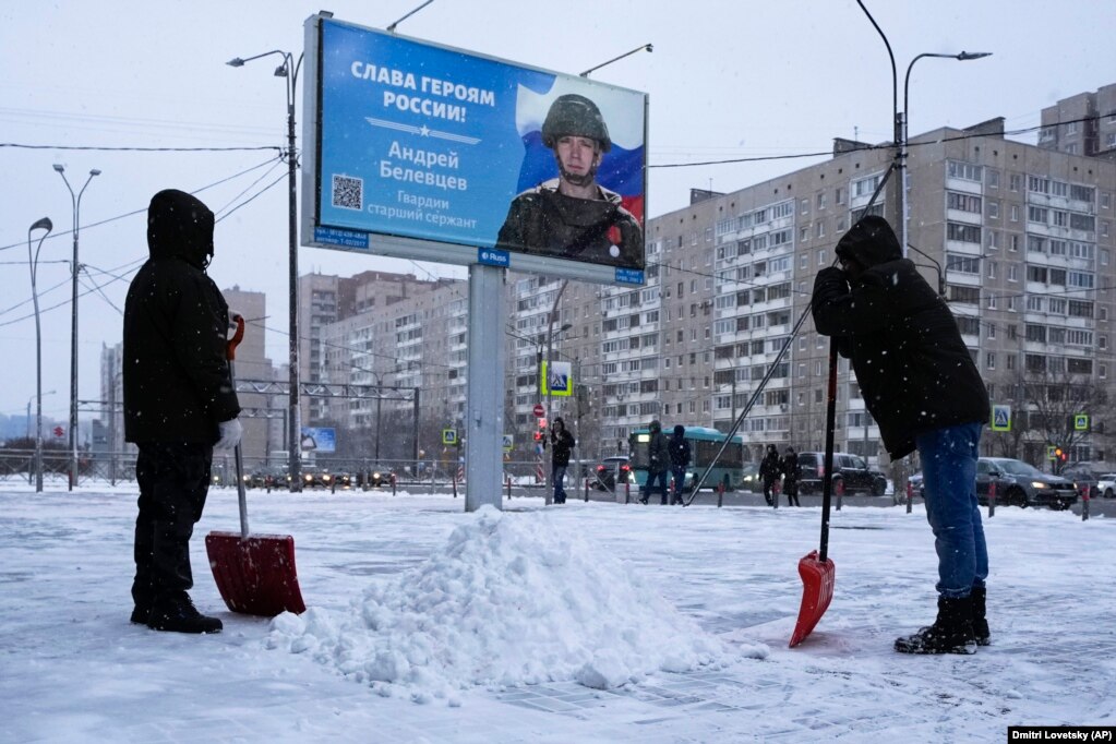 Disa punëtorë shihen duke pastruar borën në Shën Petersburg afër një baneri me mbishkrimin &ldquo;Lavdi heronjve të Rusisë&rdquo;.