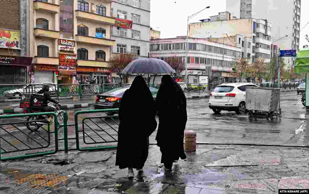 Two Iranian women share an umbrella as they stand on a square in Tehran.