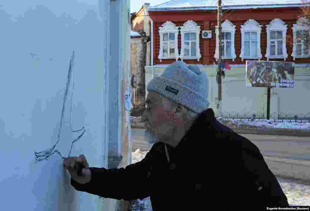 A billboard promoting the Russian armed forces stands in the background as&nbsp;Ovchinnikov paints a new mural in Borovska on December 7. Ovchinnikov told Reuters that his mural of the Ukrainian girl was painted over and he was ordered to pay a 35,000-ruble ($554) fine for the offense of &quot;discrediting the Russian military,&quot; which carries a maximum penalty of five years in prison. &nbsp;