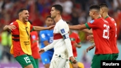 Чемпионат мира по футболу FIFA 2022 в Катаре, в четвертьфинале Марокко – Португалия. Доха, 10 декабря 2022 года. Португалец Криштиану Роналду выглядит удрученным после вылета из чемпионата мира, а игроки Марокко празднуют выход в полуфинал.