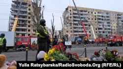 Люди несуть квіти, свічки та іграшки до будинку, зруйнованого російською ракетою, Дніпро, 16 січня 2023 року