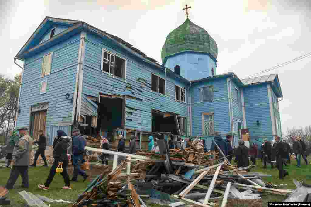 Banorët vendës duke u larguar pas shërbesës për Pashkët Ortodokse, në oborrin e Kishës së Virgjëreshës së Shenjtë, e cila është dëmtuar nga bombardimet në fshatin Peremoha.