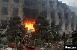 Orosz és csecse katonák a mariupoli Azovstal acélgyár megsemmisített adminisztratív épülete előtt 2022. április 21-én