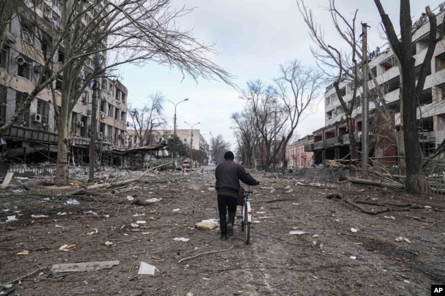 Háborús pusztítás, háborús bűnök – egy biciklit tol a szétlőtt Mariupolban 2022. március 10-én