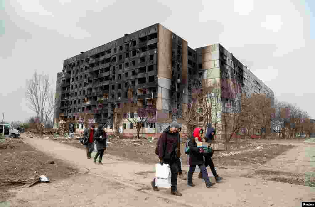 Kiégett lakóházak előtt sétálnak el civilek. A G7-országok vezetői csütörtöki&nbsp;külügyminiszteri ülésük után&nbsp;határozottan elítélték a civilek elleni, válogatás nélküli támadásokat, így Mariupol és más városok ostromát is