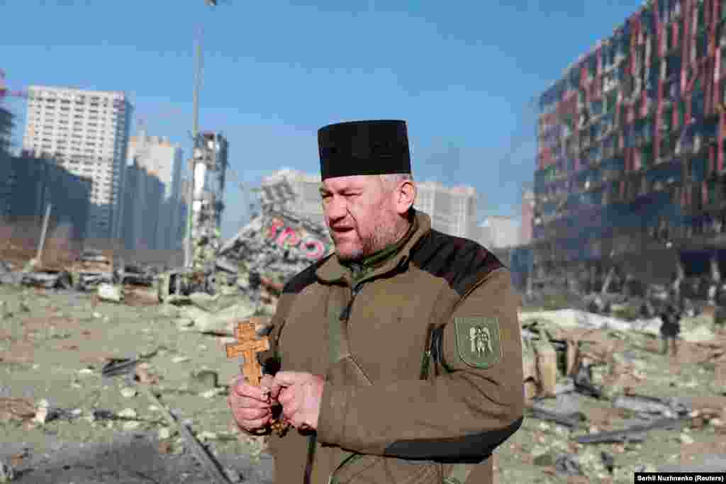 A chaplain holds a cross and rosary beads at the site of a Russian air strike on a shopping center in Kyiv.&nbsp;