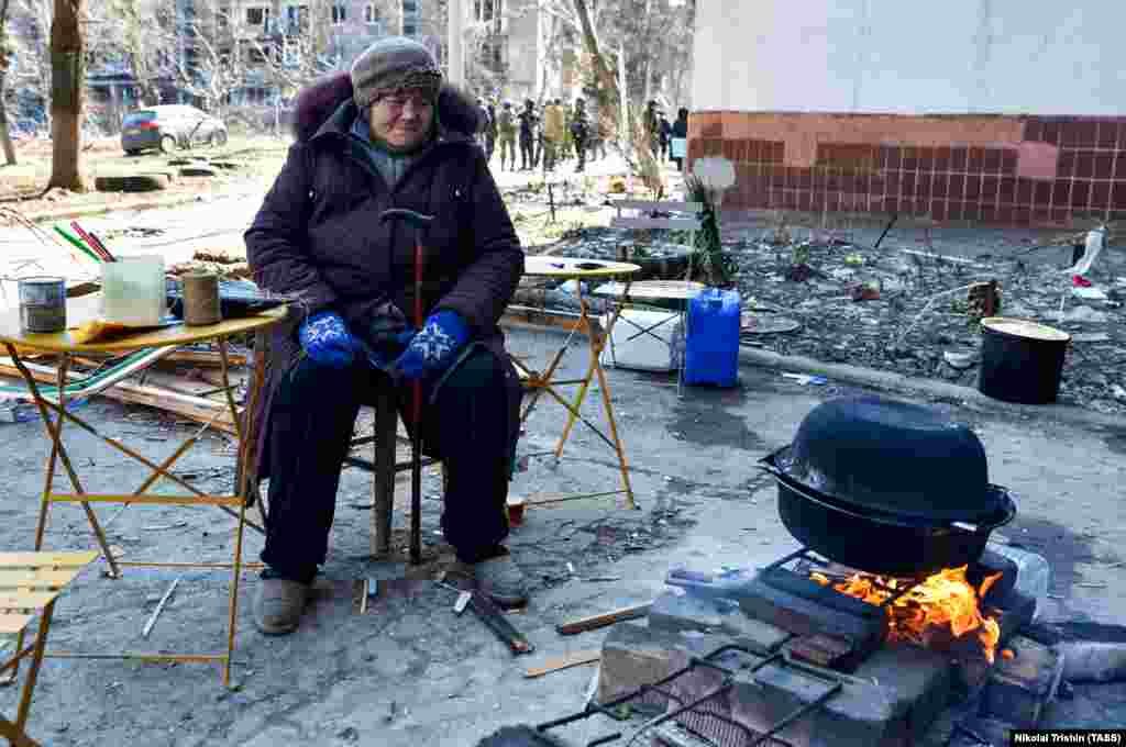 Женщина готовит еду на костре рядом с жилым районом, пострадавшим от российского обстрела. Некоторые растапливают снег, питьевой воды в городе нет