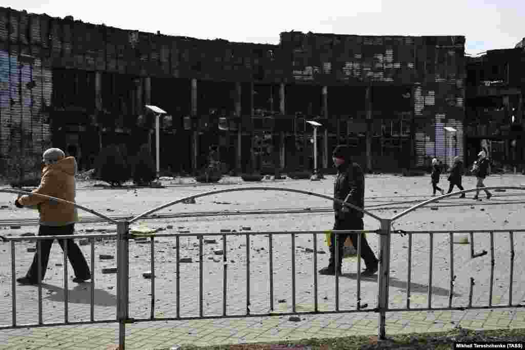 Граѓани поминуваат покрај трговскиот центар уништен од гранатирање во Мариупол, 20 март 2022 година.