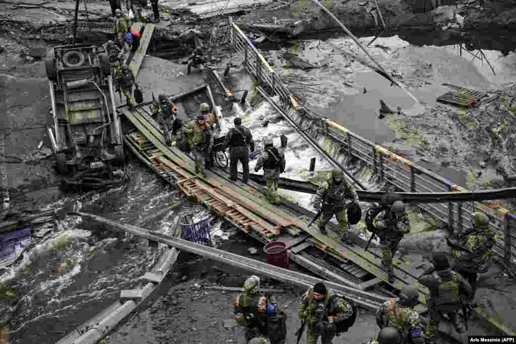 Ukrainian servicemen cross a river next to a destroyed bridge near the city of Irpin on March 13.&nbsp;