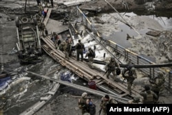 Військовослужбовці ЗСУ перетинають річку через зруйнований міст поблизу міста Ірпінь на Київщині, 13 березня 2022 року