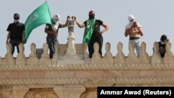 Palestinac drži zastavu Hamasa dok stoji pored drugih na vrhu džamije Al-Aksa nakon sukoba s izraelskom policijom u kompleksu u kojem se nalazi džamija, poznatom muslimanima kao Plemenito utočište, a Jevrejima kao Brdo hrama, Stari grad Jerusalim, maj 2021.