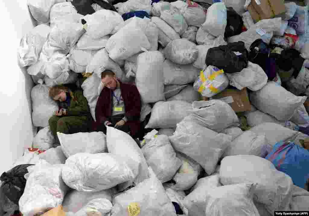 Втомлені волонтери відпочивають під час перерви на мішках з одягом, який вони мають розсортувати і роздати. Львів, 19 березня 2022 року