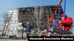 Деца играат пред оштетна зграда од руските напади врз Мариупол 