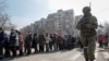 A Russian soldier stands next to local residents waiting in line for humanitarian aid in the besieged southern port of Mariupol on March 23.