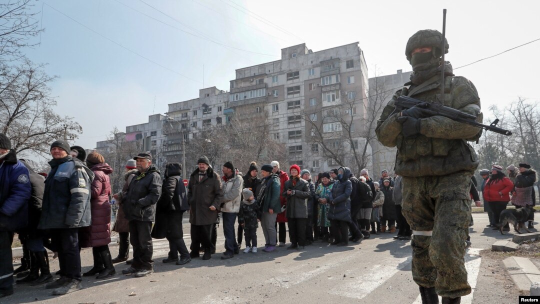 A Russian soldier stands next to local residents waiting in line for humanitarian aid in the besieged southern port of Mariupol on March 23.