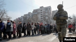 A Russian soldier stands next to local residents waiting in line for humanitarian aid in the besieged southern port of Mariupol on March 23.