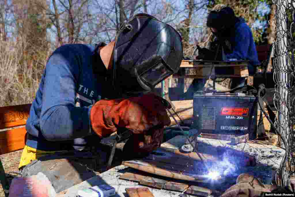Férfiak dolgoznak az ukrán védelmi erők tagjainak laprugóból készülő golyóálló mellényeinek lemezein