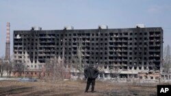 Un bărbat se uită la un bloc de apartamente incendiat care a fost avariat de bombardamente în Mariupol pe 13 martie. Foto: AP

