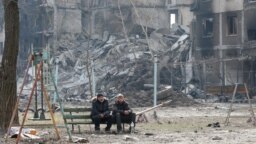 Local residents sit on a bench near a destroyed apartment building in Mariupol on March 25. 