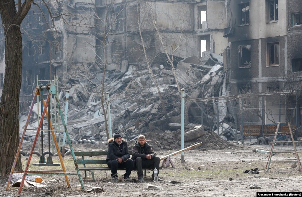 Local residents sit on a bench near a destroyed apartment building destroyed in Mariupol on March 25.