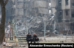 Local residents sit on a bench near a destroyed apartment building destroyed in Mariupol on March 25.