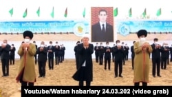 Oficiali turkmeni pe fundalul unei imagini a președintelui Serdar Berdîmuhamedov, care a preluat funcția de la tatăl său, în martie 2022. 