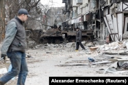 Жители на Мариупол минават покрай унищожена бронирана техника, 25 март 2022 г.