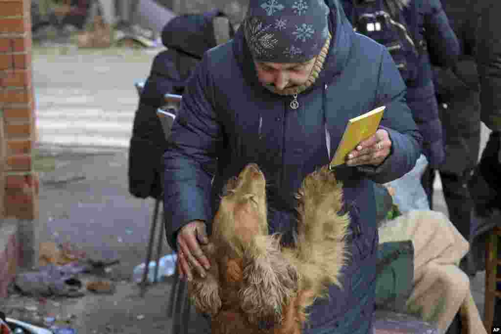 Egy nő simogatja a kutyáját Bibliával a kezében egy ellenőrző ponton Mariupol külvárosában március 27-én