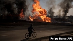 Велосипедист на фоне горящего здания после российского обстрела. Харьков, март 2022 г.