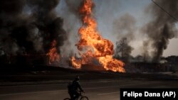 УКРАИНА - Човек вози велосипед покрај пламен и чад што се издига од пожар по руски напад во Харкив. 25.03.2022
