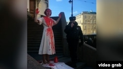 A St. Petersburg artist doused herself in red paint and chanted “My heart bleeds” in front of the city’s legislature on March 27 before being taken away by police.