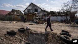 Čovek hoda iza kratera nastalog od bombe i ispred oštećenih kuća nakon ruskog bombardovanja na periferiji Mikolajeva.