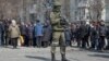 A Russian soldier stands next to local residents waiting in line for humanitarian aid in the besieged southern Ukrainian port of Mariupol. 