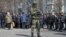 A Russian soldier stands next to local residents waiting in line for humanitarian aid in the besieged southern Ukrainian port of Mariupol. 