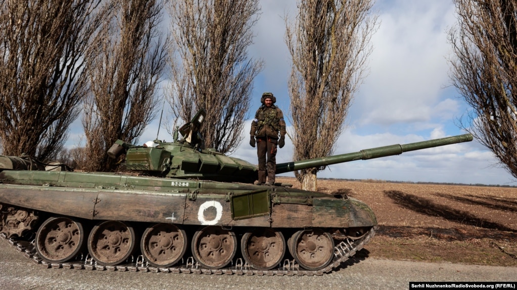 Український військовослужбовець стоїть на захопленому бою російським танком Т-72 у селі Лук'янівка, що на Київщині, 27 березня 2022 року