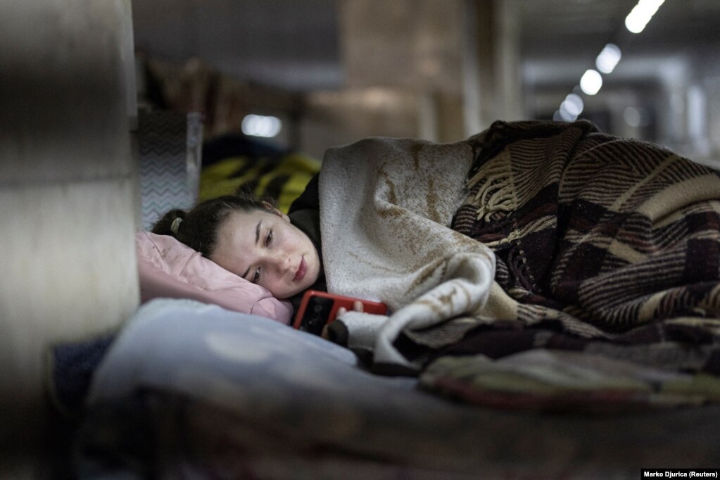 Masha, 26-vjeçare, duke shikuar telefonin e saj mobil, në një stacion metroje, që shërben si strehim nga sulmet e mundshme ajrore, teksa pushtimi rus i Ukrainës po vazhdon. (Kiev, 25 mars)