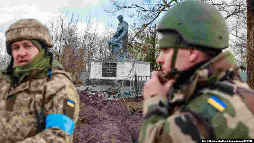 Ukrainian soldiers stand next to the damaged memorial to the fallen soldiers of World War II in Lukyanivka
