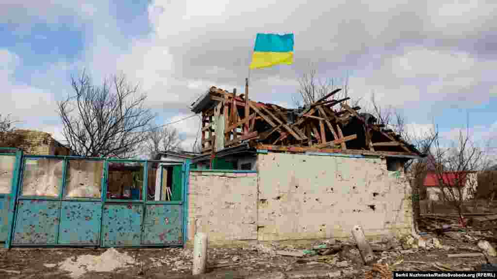 The Ukrainian flag flies above a destroyed home.