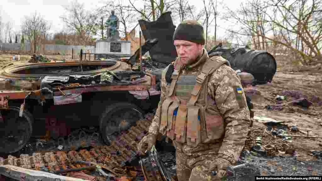 Ukrán katona és egy megsemmisített orosz tank Lukjanivkában március 27-én