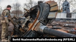Военнослужащий Украины осматривает остатки уничтоженного российского танка, село Лукьяновка Киевская область, 27 марта 2022 года
