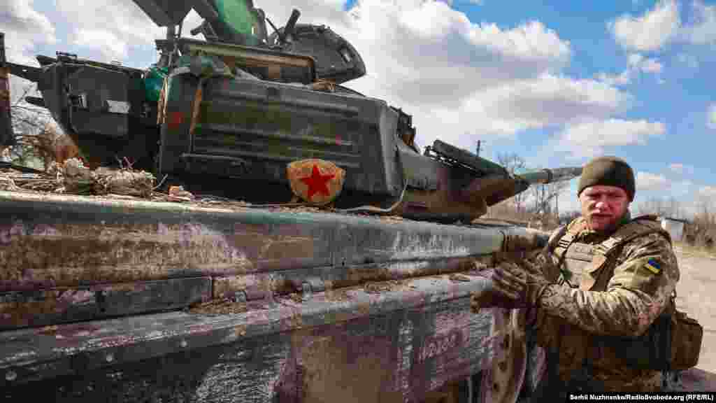 Украиналық әскери Ресей әскерилері қалдырып кеткен танкінің жанында тұр.&nbsp;