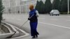 Turkmenistan. Woman with mask cleaning the street of Ashgabat. State white building. Cars. March, 2022 