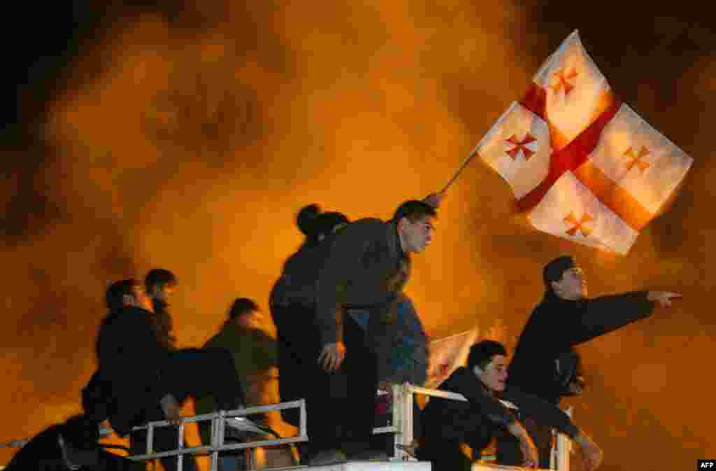 Georgian opposition supporters wave their flag at a rally in front of parliament overnight on November 23, but opposition leader Mikheil Saakashvili warned supporters that it was &quot;too early&quot; to celebrate victory after they stormed parliament, forcing the fomer Soviet republic&#39;s embattled president to flee.