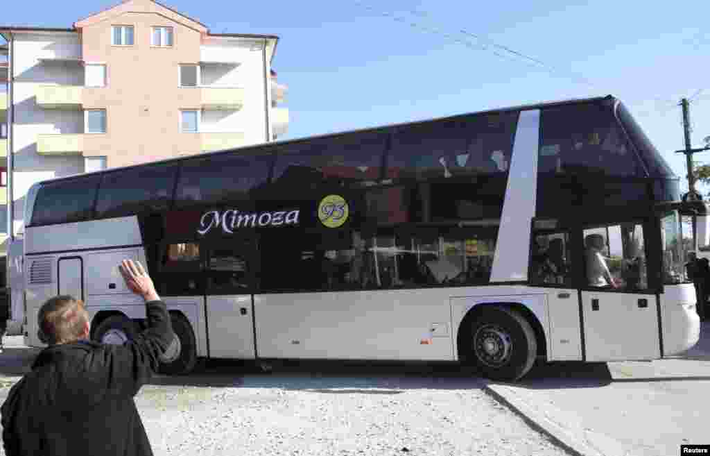 A man waves goodbye to his friends as the bus leaves.