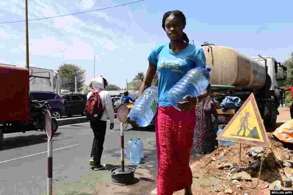 Сенегалка везет большие бутылки с водой из водовоза во время раздачи в Дакаре 8 марта 2022 года.